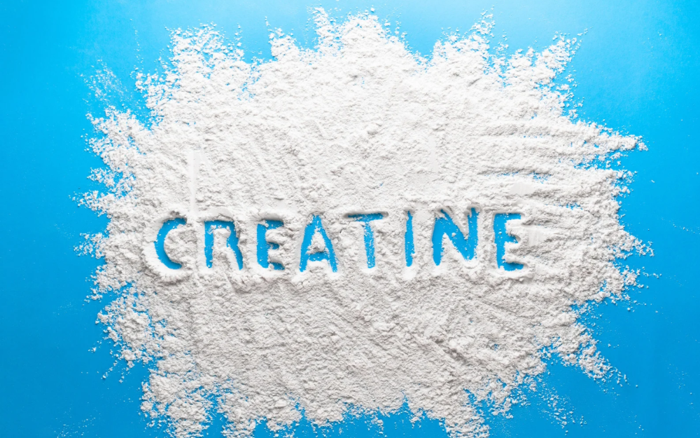 White creatine powder spread across a blue background with the word “CREATINE” written in the center—representing creatine supplements and the benefits of creatine for brain and physical health.
