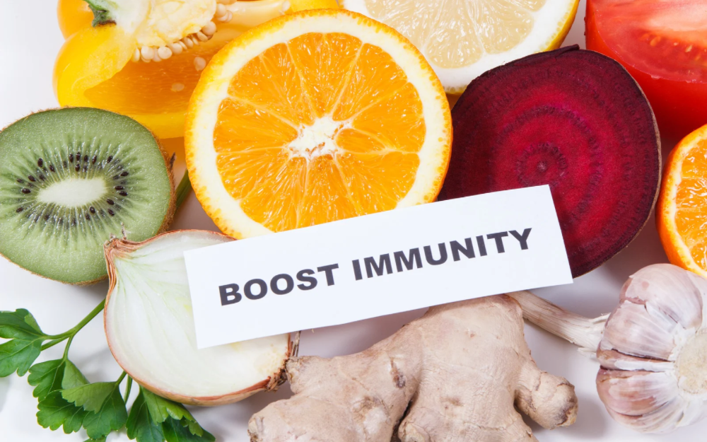 A variety of immune-boosting foods—including citrus, kiwi, beetroot, garlic, onion, and ginger—surround a label that reads “BOOST IMMUNITY,” emphasizing the role of nutrition in supporting a healthy immune system.
